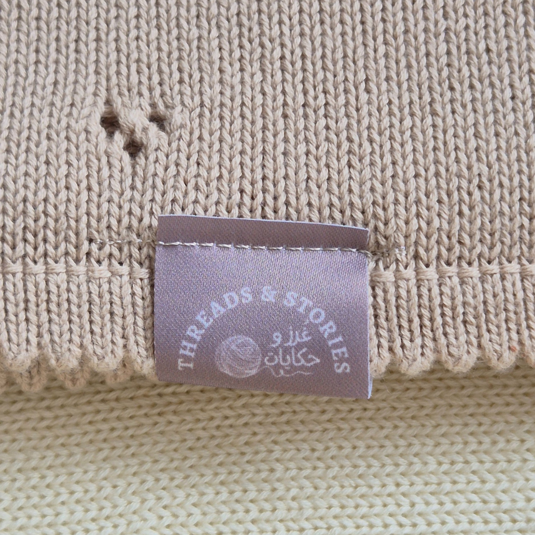 Close-up of a beige knitted fabric with a 'Threads & Stories' label.