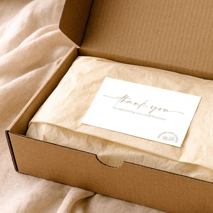 Open cardboard box with a folded white card inside on a beige fabric background